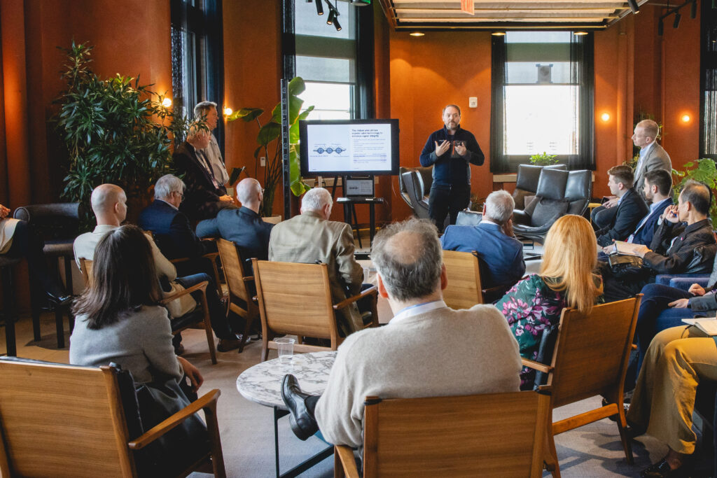 Corbin Tillemann-Dick of Maybell Quantum presents to a group of people sitting on tan chairs and couches